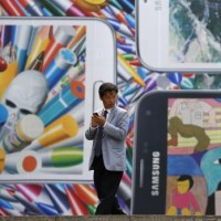 A man uses his mobile phone in front of a giant advertisement promoting Samsung Electronics‘ new Galaxy S5 smartphone, at an art hall in central Seoul