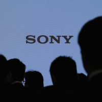 Journalists are silhouetted against a board showing Sony’s logo at its news conference in Tokyo