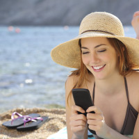 Woman on the beach texting a smart phone in summer